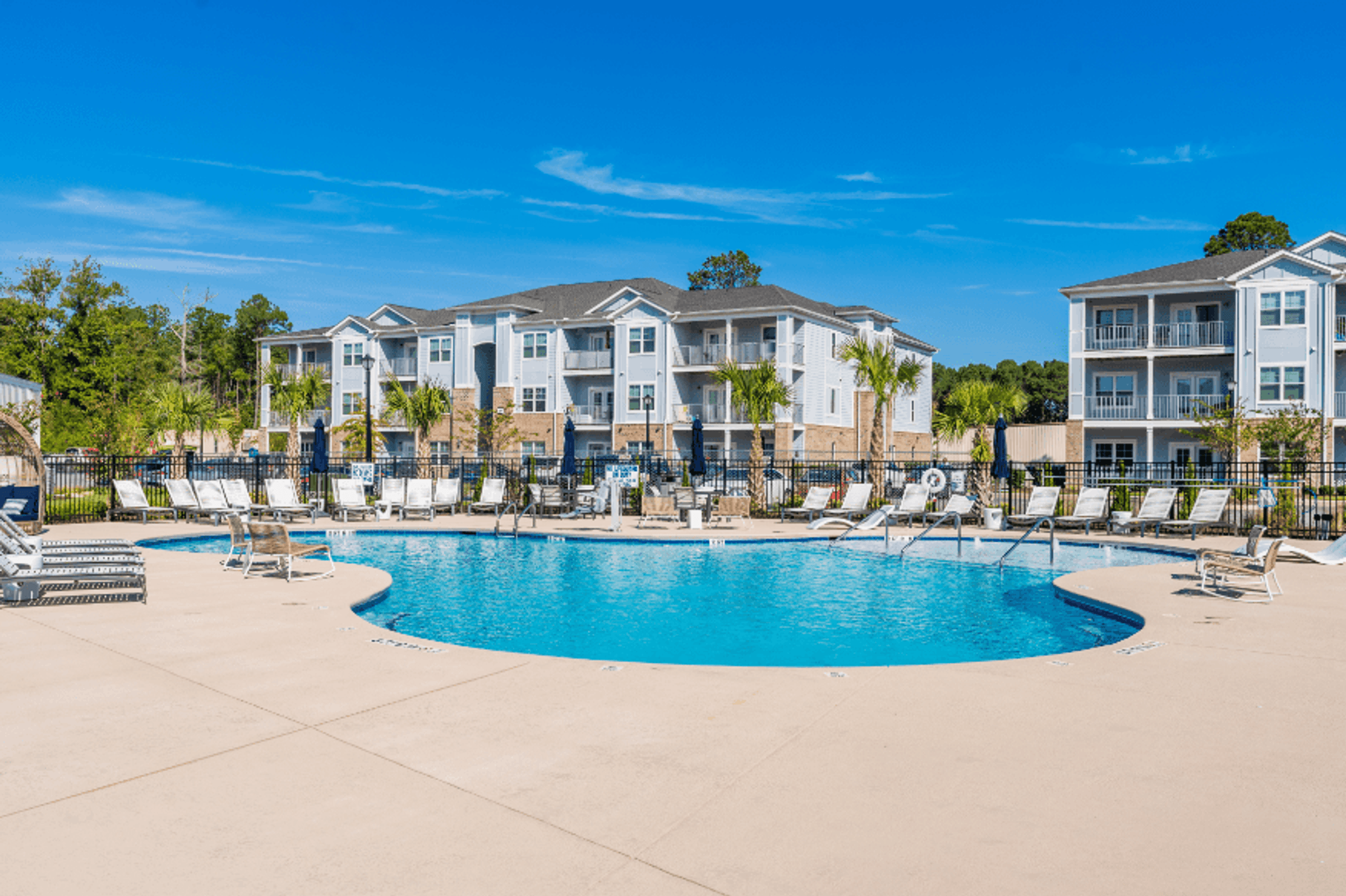 A swimming pool surrounded by lounge chairs and apartment buildings in the background