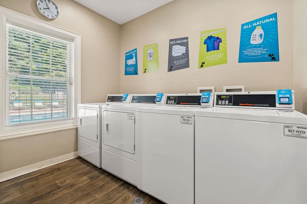a laundry room with four washers and dryers and a window and a clock