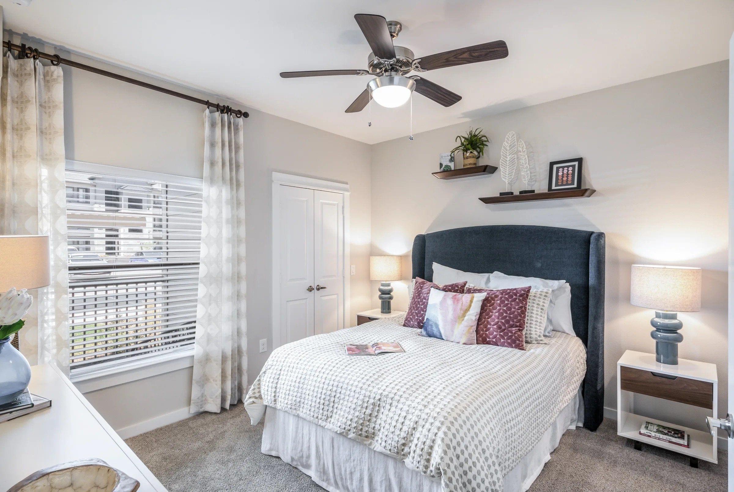 A bedroom with a bed, a ceiling fan, and a window with blinds.