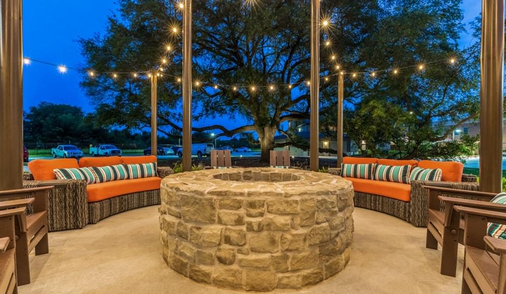 the patio of a restaurant with a stone fire pit and lights