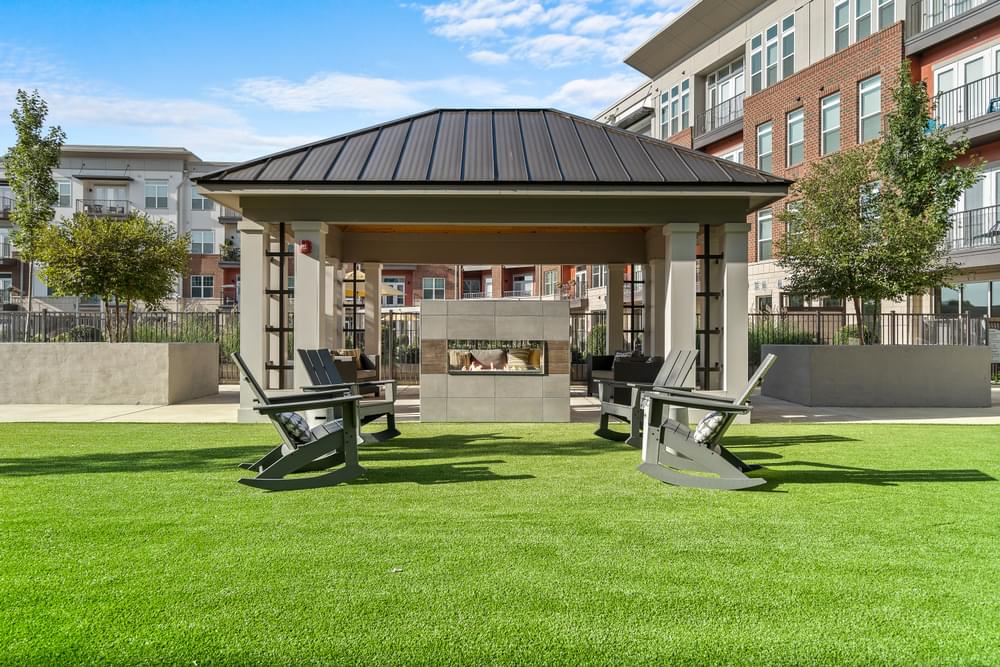a gazebo with two chairs on a lawn in front of a building
