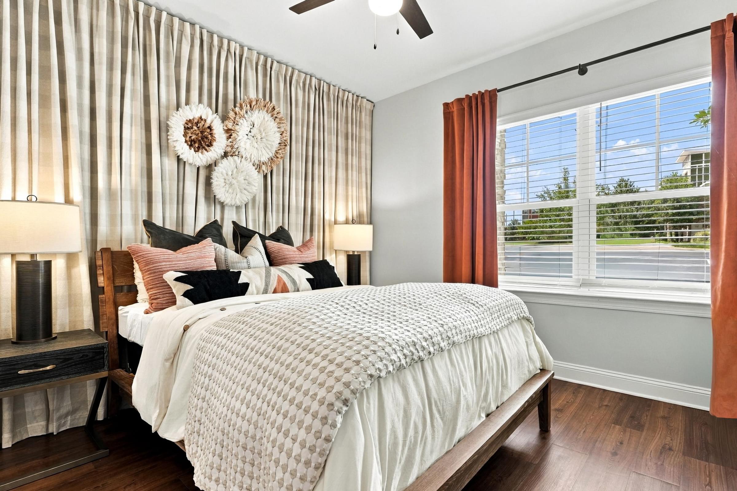 A bedroom with a large bed and a window with orange curtains.