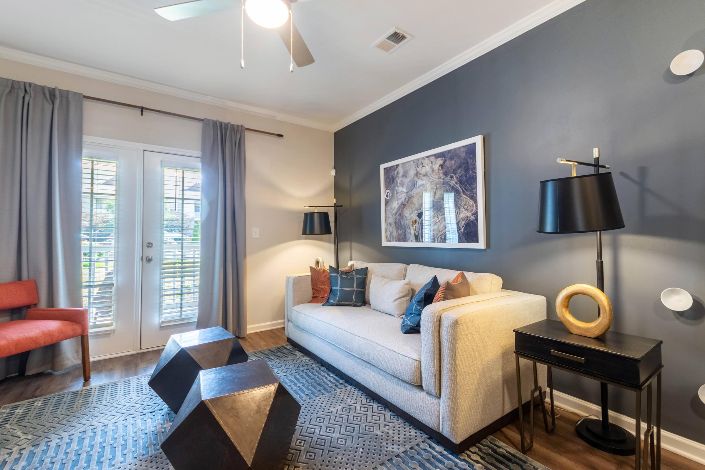 A living room with a white couch, a red chair, and a black table with a lamp on it.