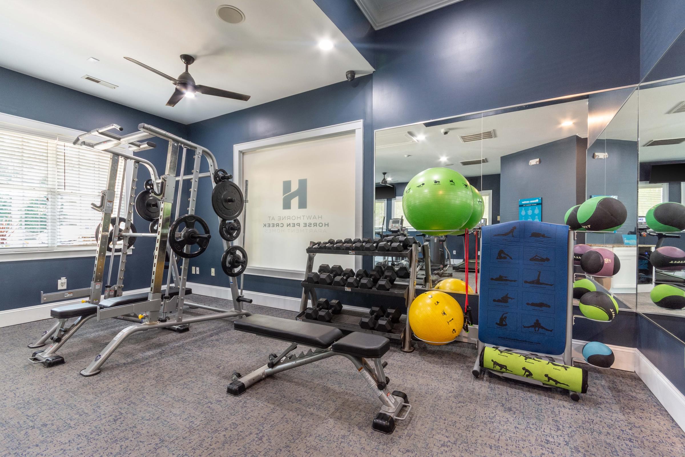 A gym room with a variety of equipment including a weight bench, a ball, and a mirror.