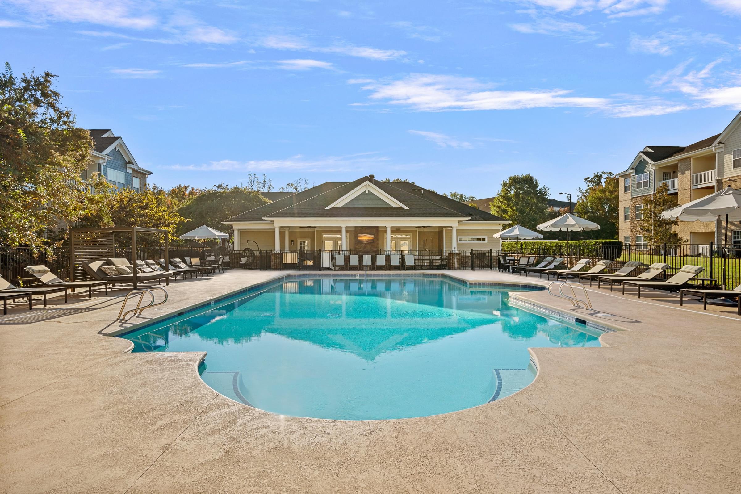 A large outdoor swimming pool surrounded by lounge chairs and a building in the background.