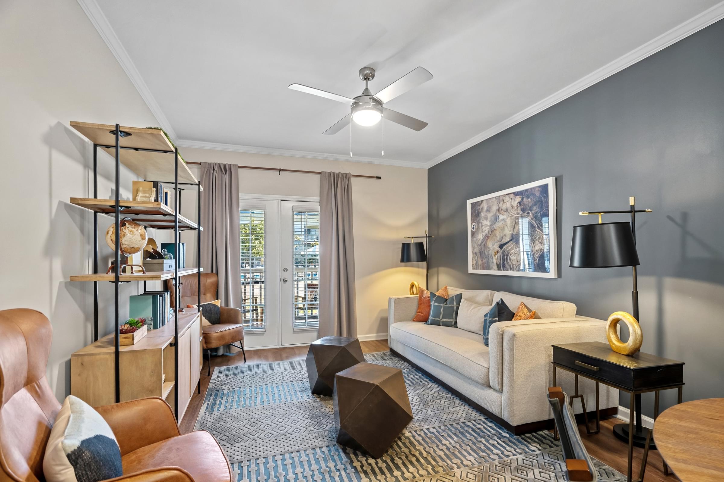 A living room with a white couch, a brown leather chair, a wooden shelf, and a ceiling fan.