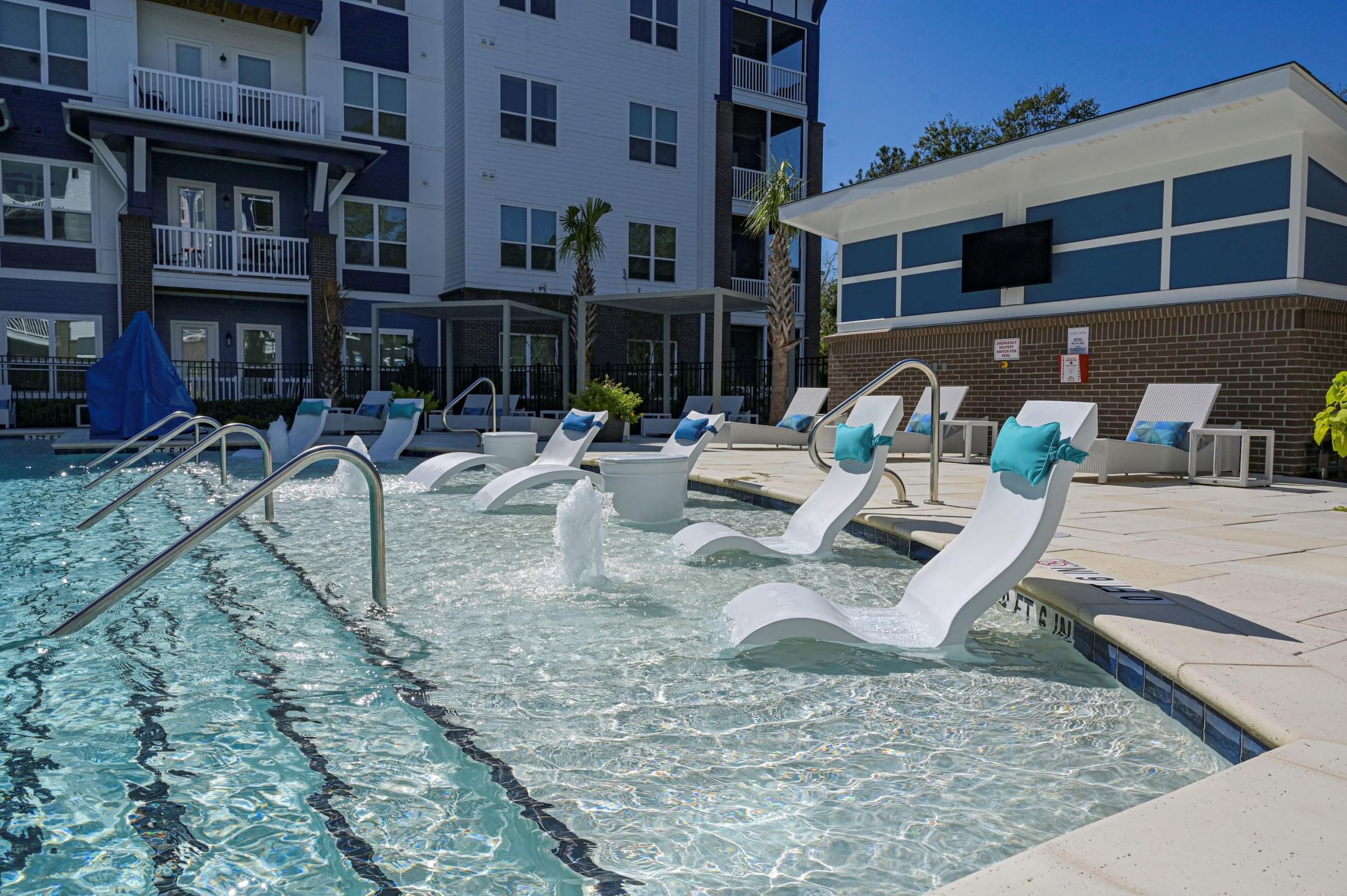 A pool with sun loungers and a building in the background.