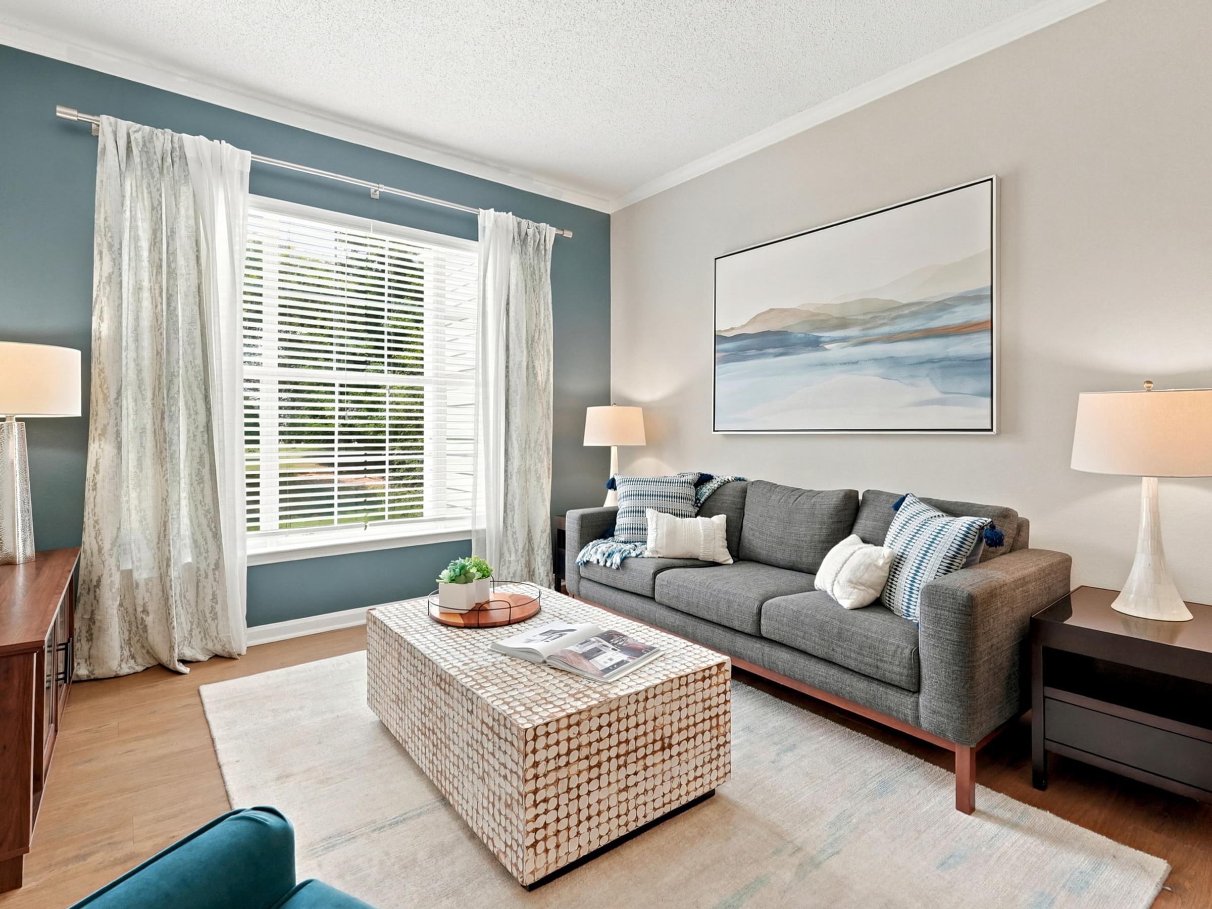 A living room with a grey couch, a coffee table, and a painting on the wall.