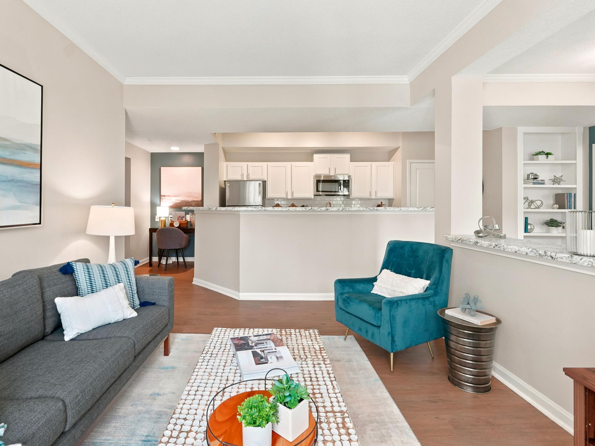 A living room with a grey couch, a blue armchair, and a coffee table with a plant on it.