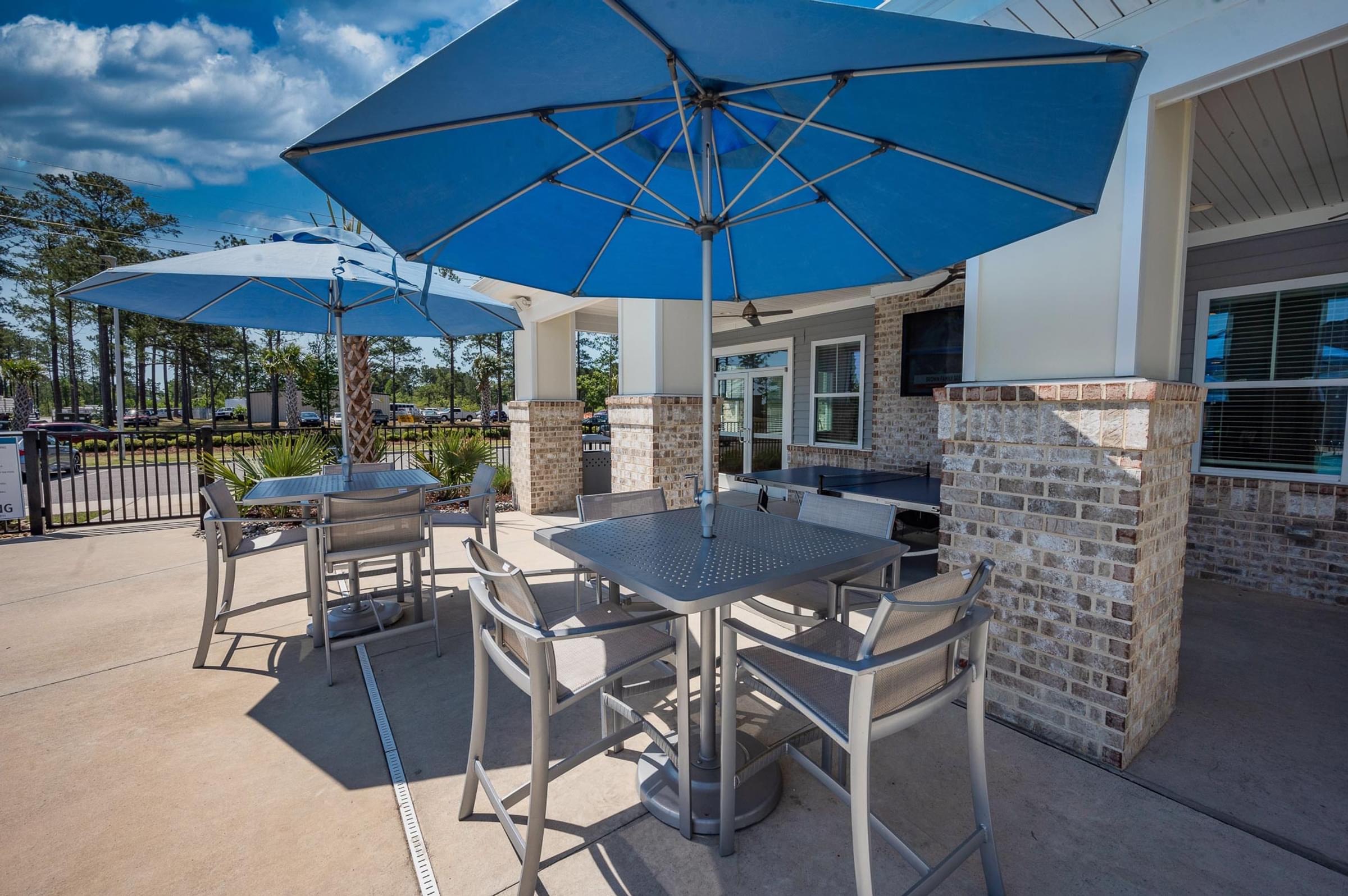 A blue umbrella shades a table with chairs outside a building.