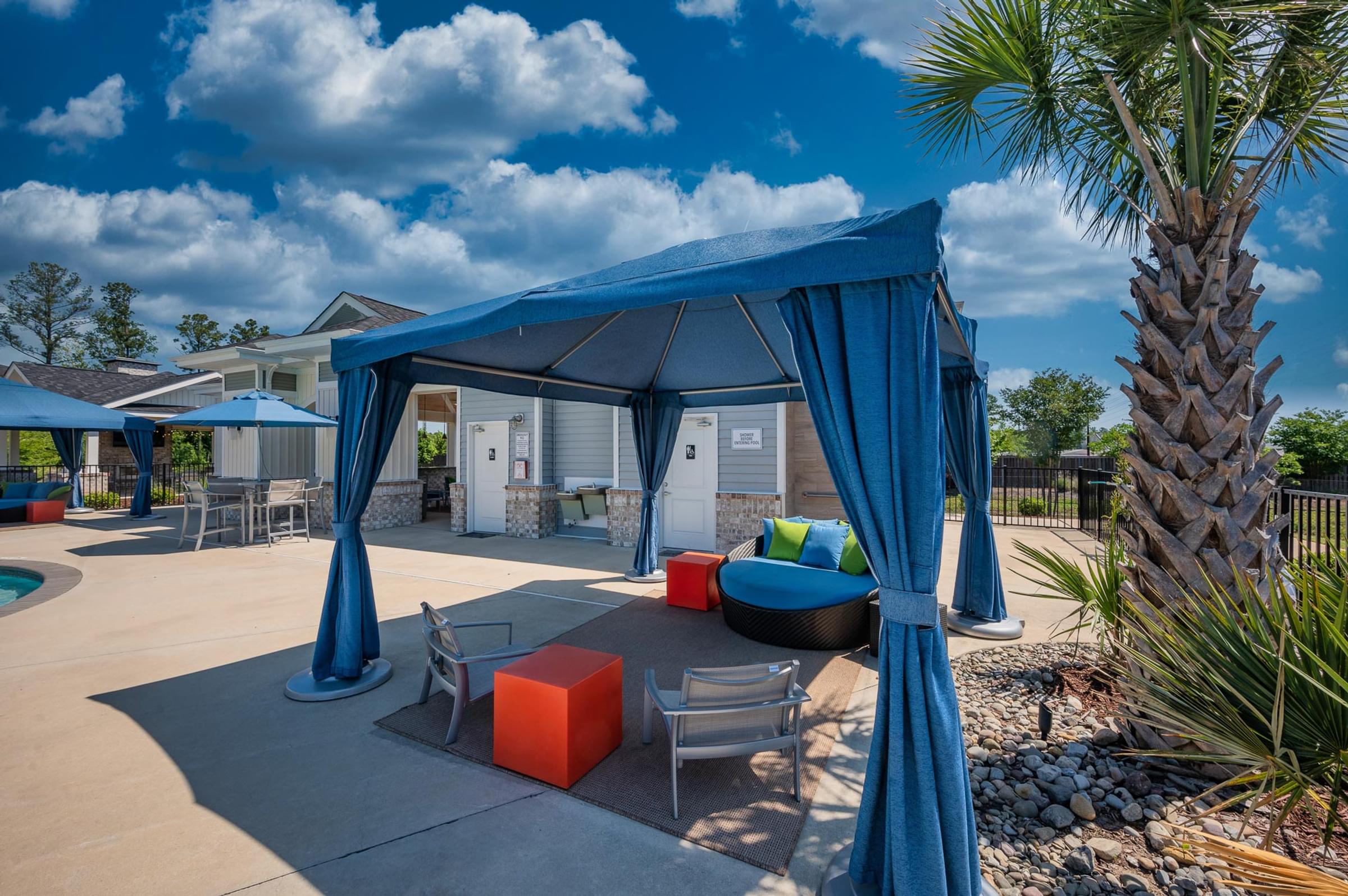 A blue canopy structure is set up in a backyard with a palm tree and a pool.