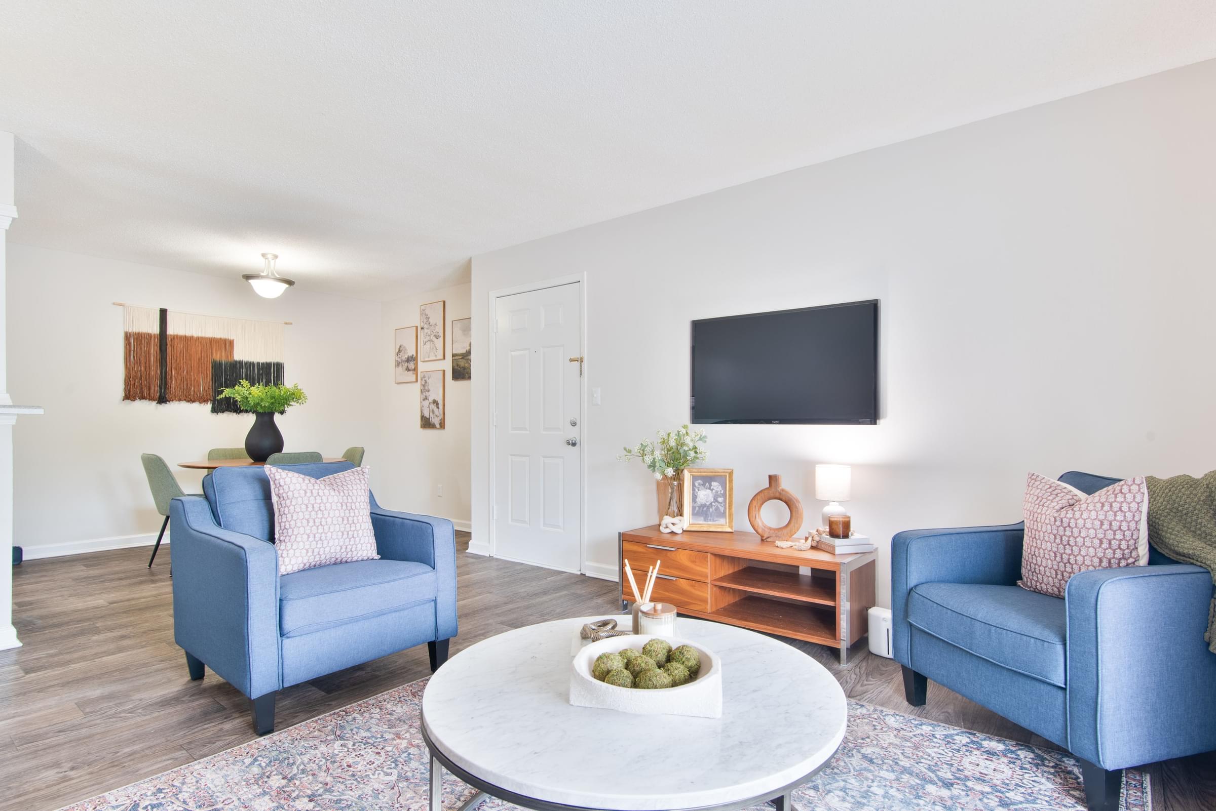 A living room with a blue couch, a white coffee table, and a flat screen TV mounted on the wall.