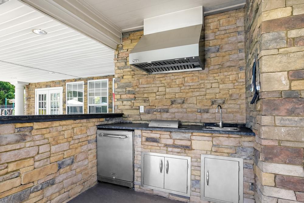 the outdoor kitchen is equipped with stainless steel appliances and a stone wall