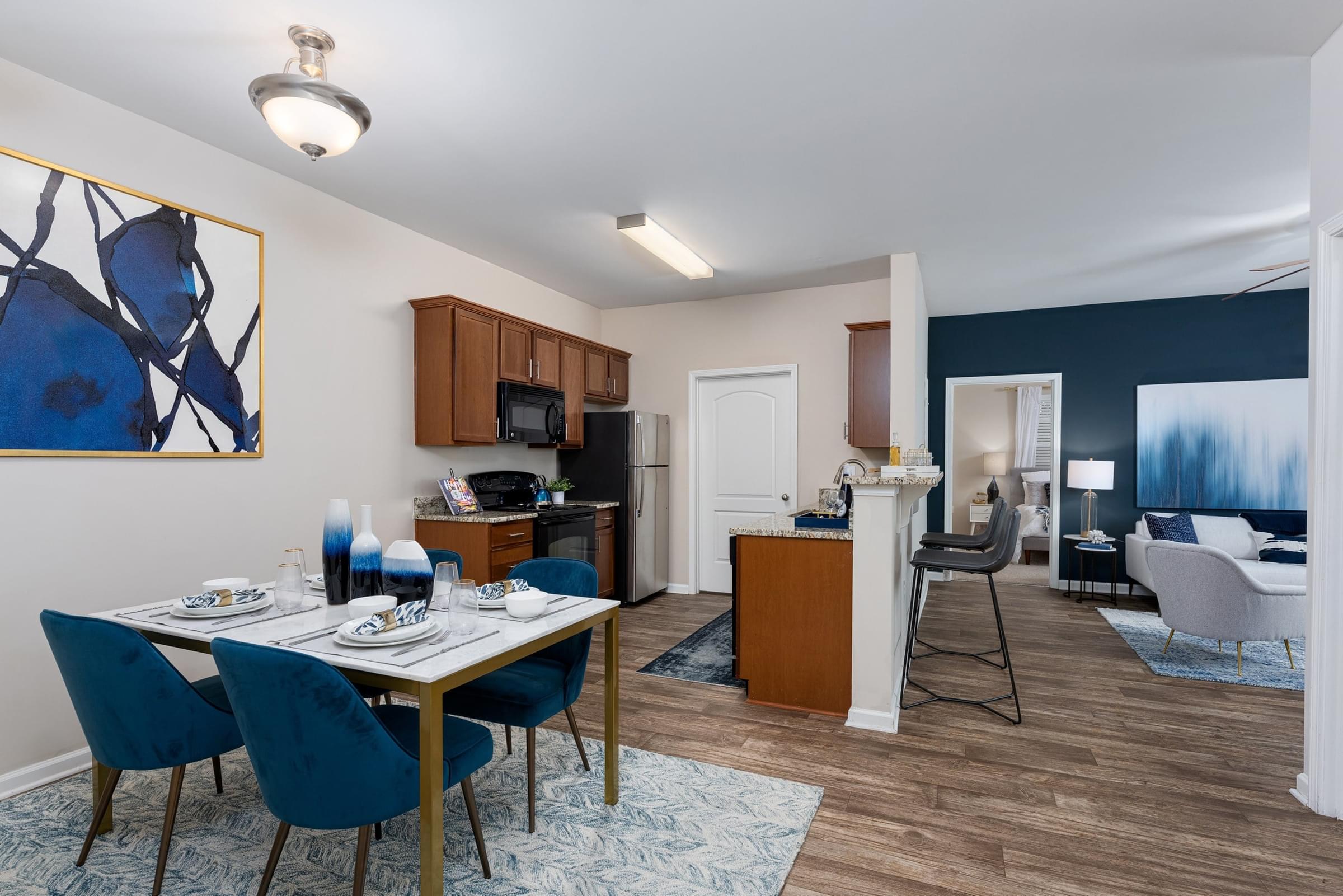 A dining room with a table set for four and a kitchen area in the background.