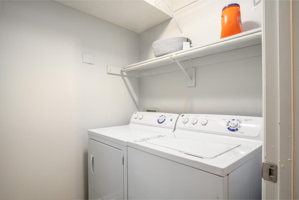 a white washer and dryer in a white room with a shelf above it