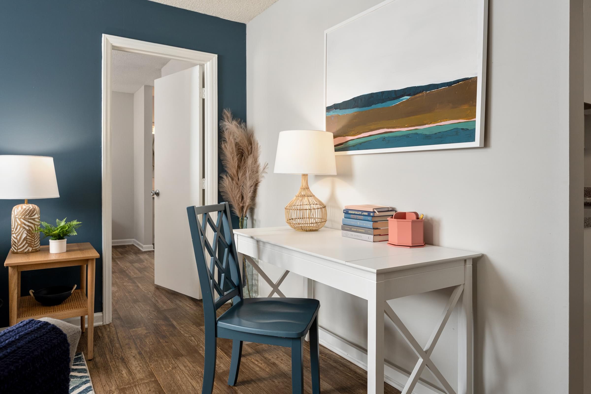 A room with a blue chair and a white desk with a lamp on it.