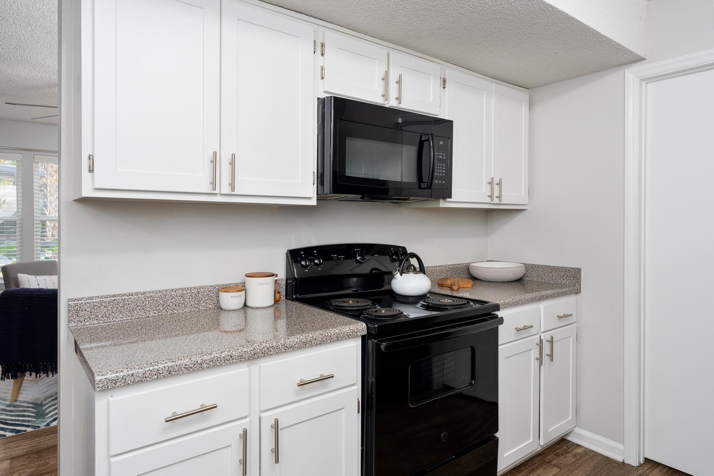 A black microwave is mounted above a black stove in a kitchen with white cabinets.