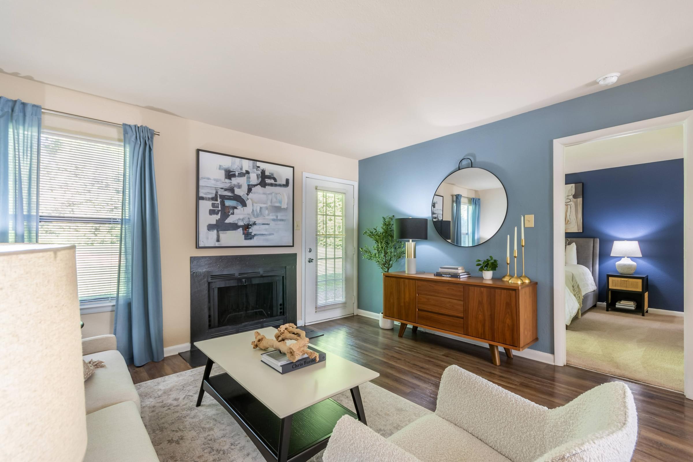 A living room with a fireplace, a chair, a couch, a coffee table, and a mirror at Hawthorne at Oak Ridge in Greensboro, NC.