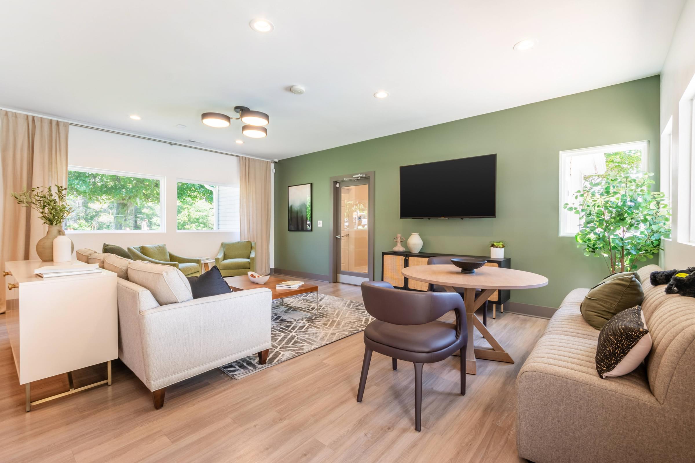 A seating area with a white sofa, a brown chair, a wooden floor, and a flat-screen TV mounted on the wall at Hawthorne at Oak Ridge in Greensboro, NC.