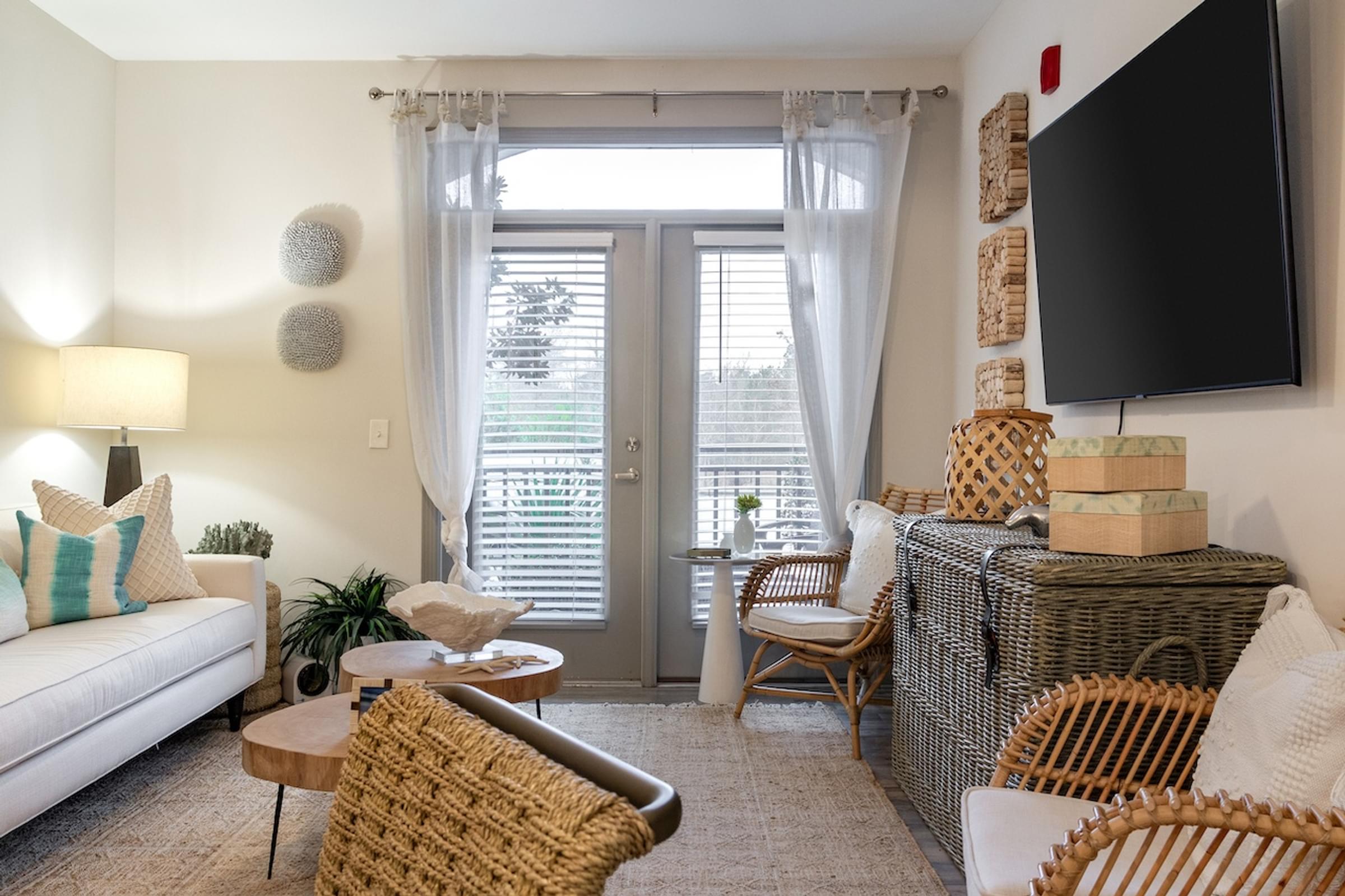 A living room with a white couch, a wicker chair, and a television mounted on the wall.
