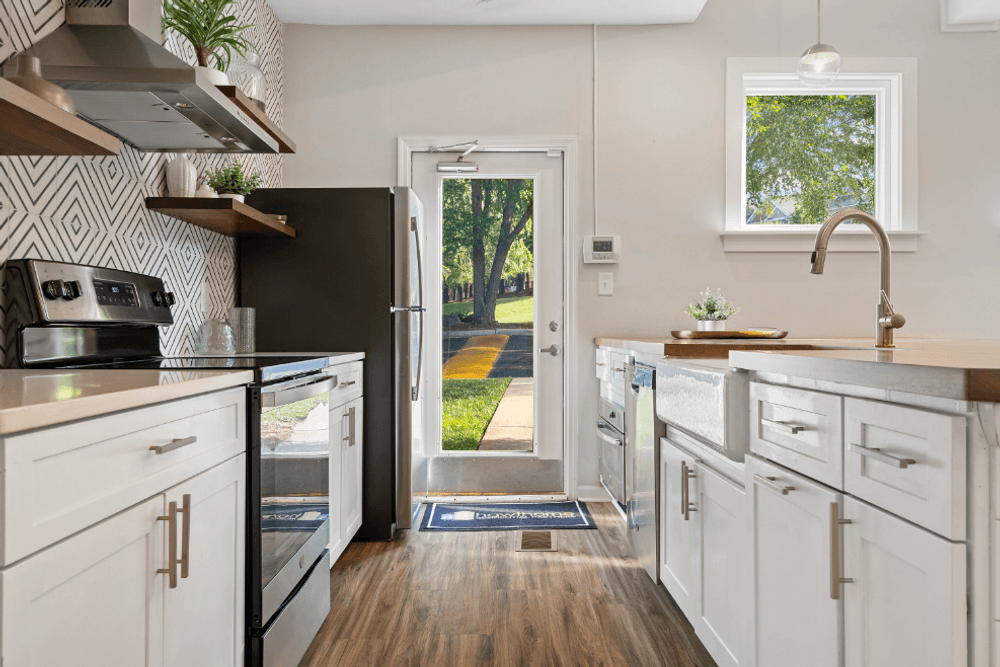 a kitchen with white cabinets and stainless steel appliances and a backdoor to a yard