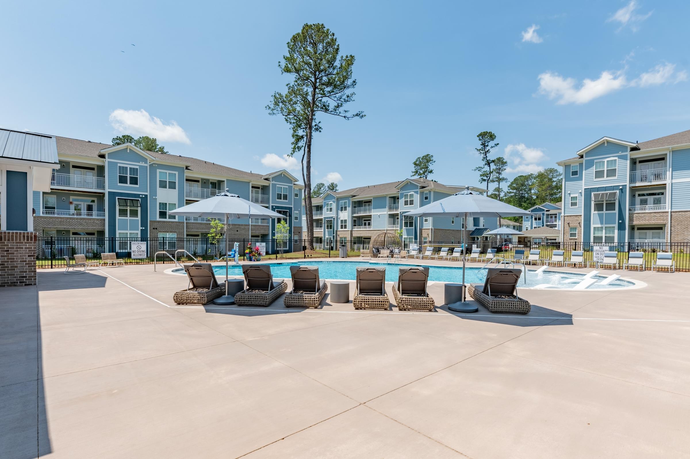 a pool with lounge chairs and umbrellas in front of an apartment building