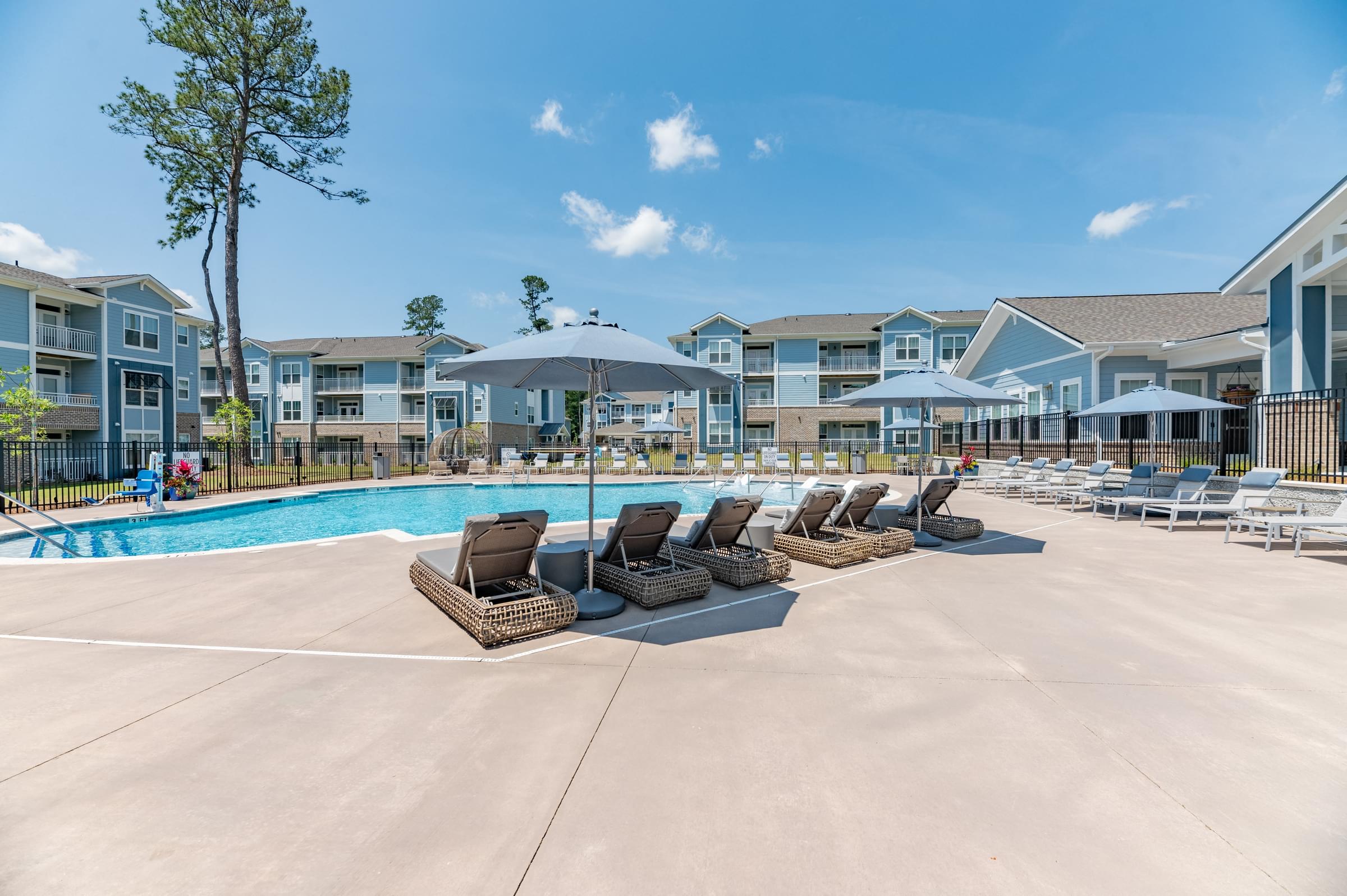 A swimming pool area with lounge chairs and apartment buildings in the background.