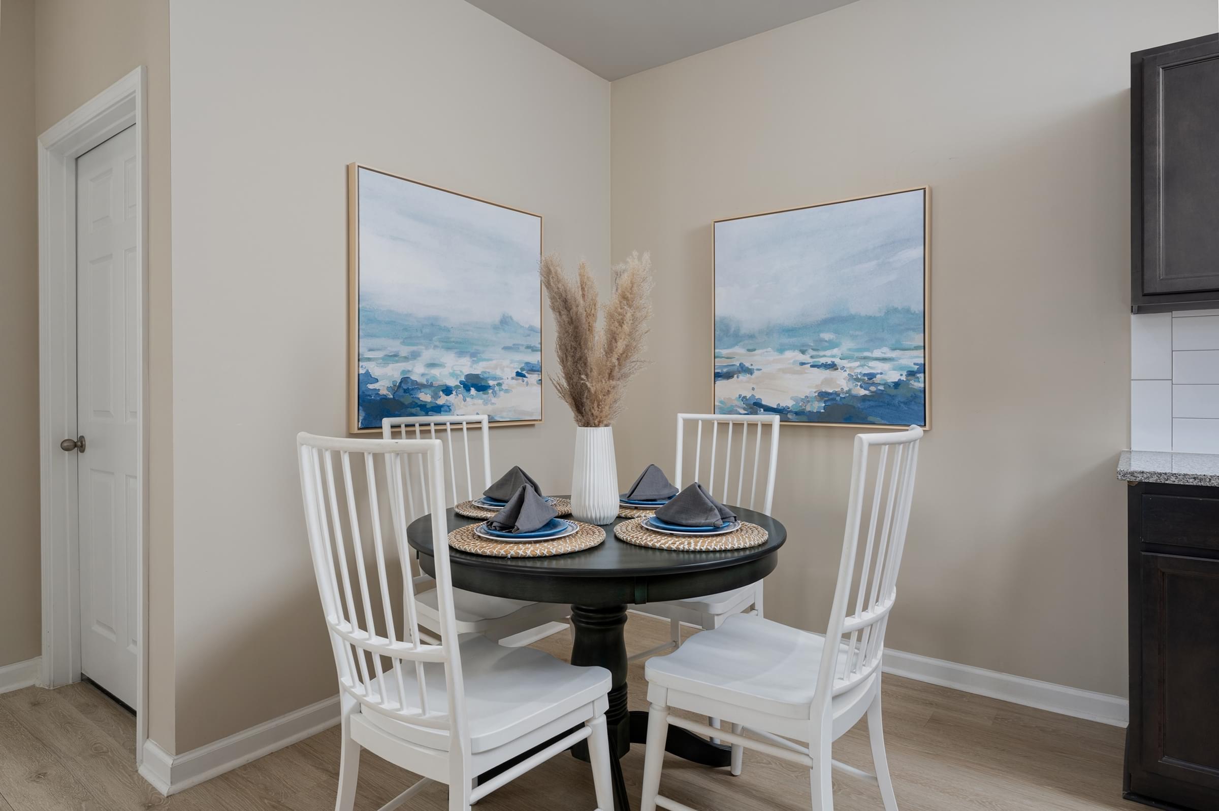 A dining room with a table set for two and two landscape paintings on the wall.