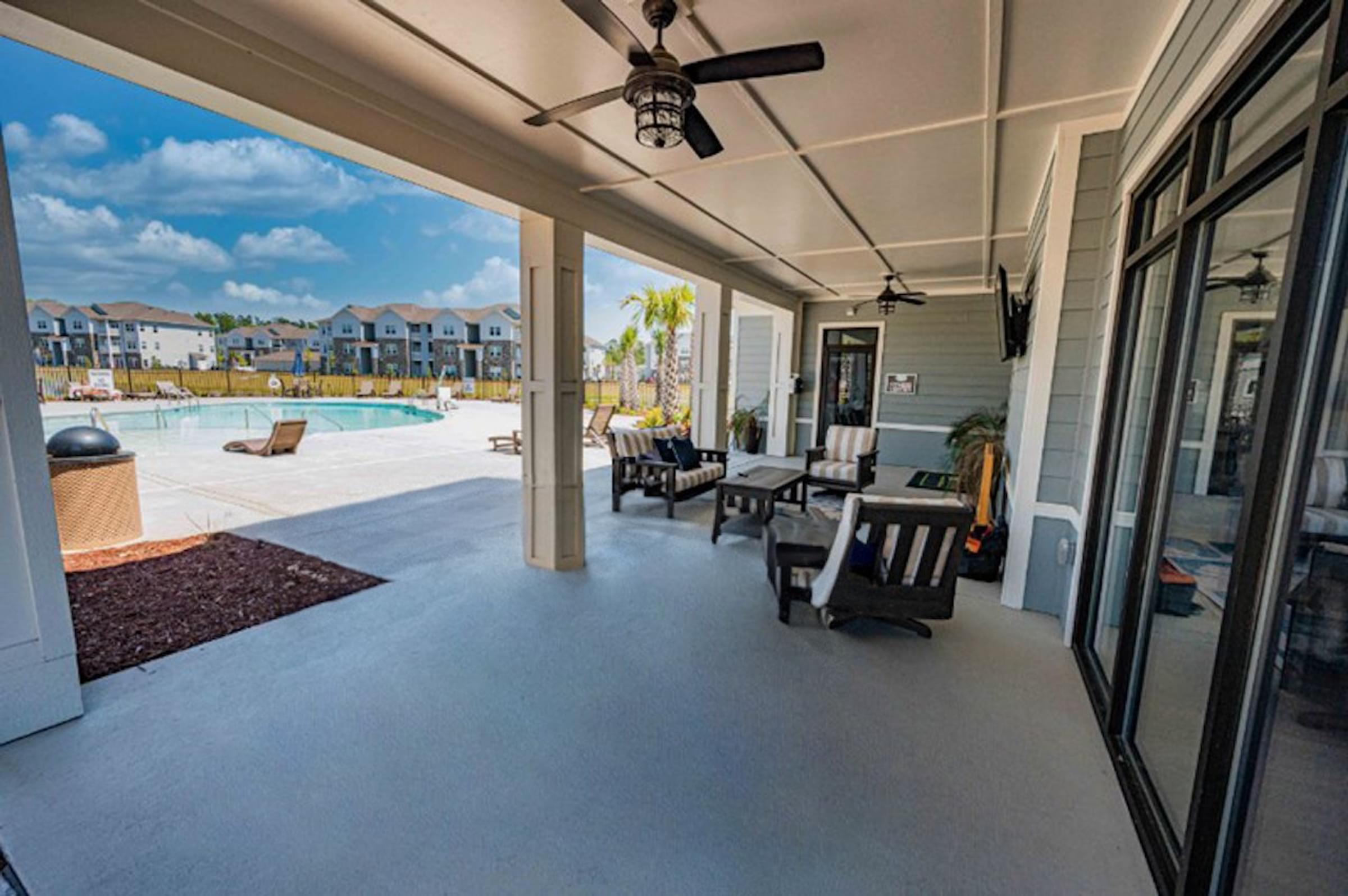 a covered porch with a pool and chairs and a ceiling fan