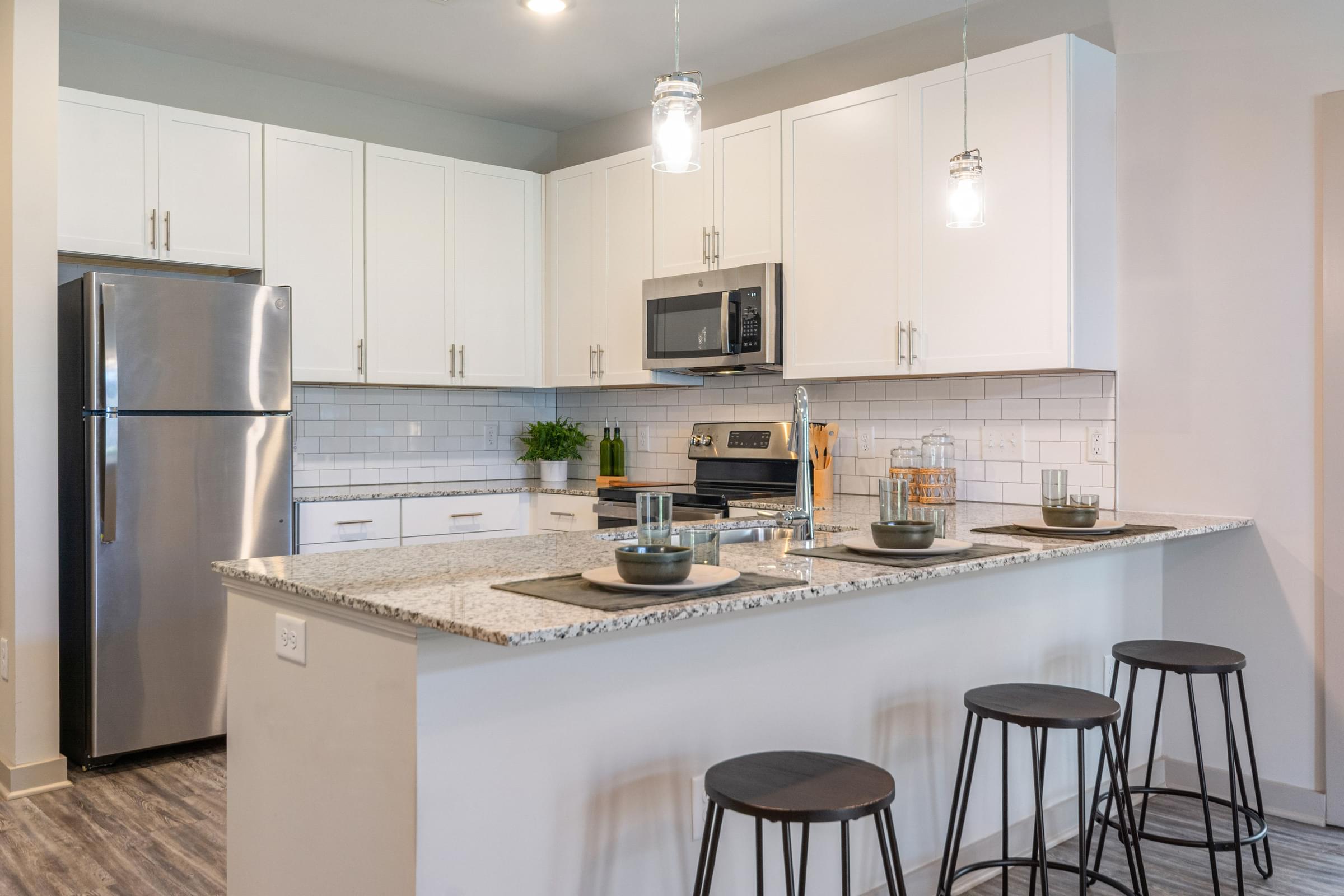 A kitchen with a refrigerator, microwave, and bar stools at Hawthorne St. Marks in Burlington, NC