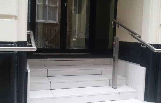 The Sesame Mayfair Stairlift clad in stone. Ithe stairs are extended over the hidden stairlift sitting below. A button post sits on the side of the staircase next to the handrails.
