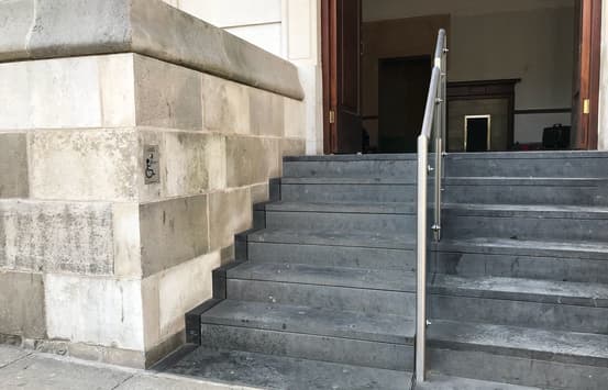 Grey steps with a stainless steel handrail seperating the two sides of the staircase with a Sesame Listed Building Lift on the left hand side.