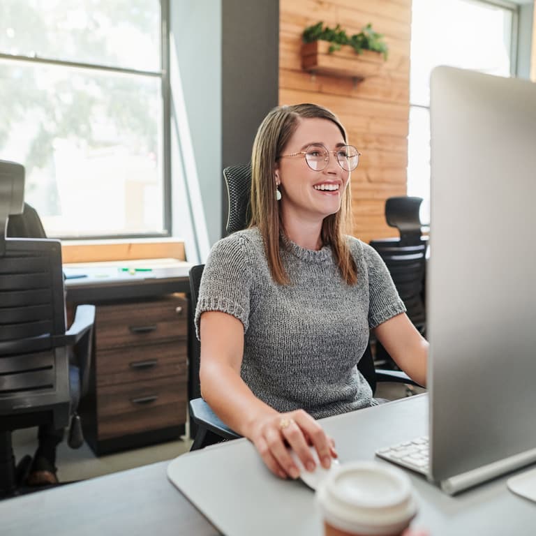 Worker sits at their desk, smiling at a computer screen