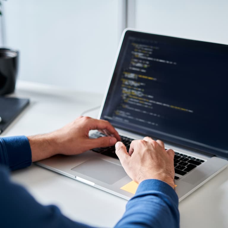 A person's hands are seen typing code on a laptop