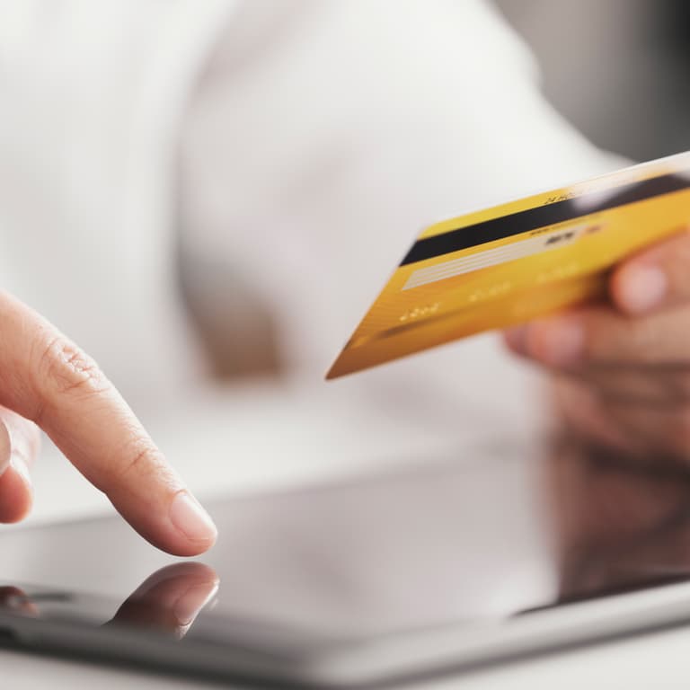 Person holds a credit card and inputs their card details into a mobile tablet