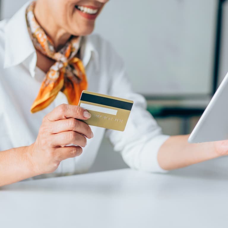 Person wearing an ascot holds a credit card in one hand and a tablet in the other