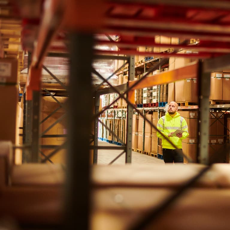 Worker in a wholesale distribution center walks down an aisle with a clipboard