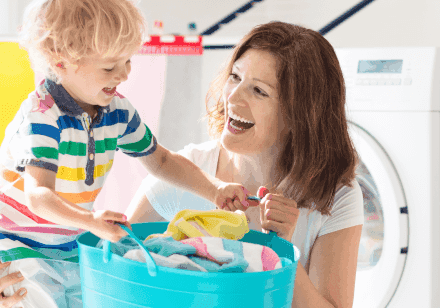 A woman and her young son are holding a laundry basket in a laundry room.