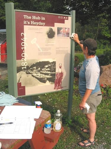 Volunteer cleaning one of the historic panels along the D&amp;H trail