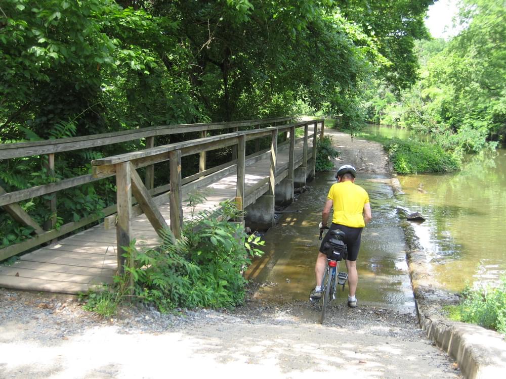Concrete trail crossing with flowing water paralleled by bridge on the C and O Canal Trail in Washington, DC