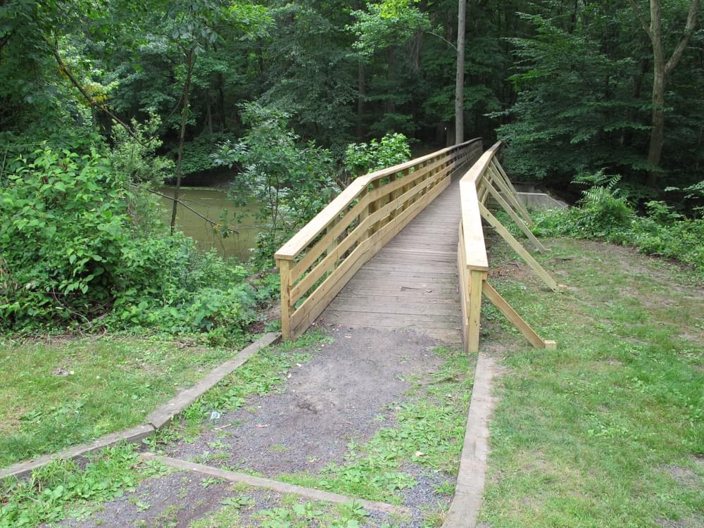 Good example of an accessible trail bridge meeting the natural surface trail. Both bridges are actually below the trail grade and material does not wash away from the bridge; Barclay Farm National Recreation Trail, Cherry Hill Township, New Jersey