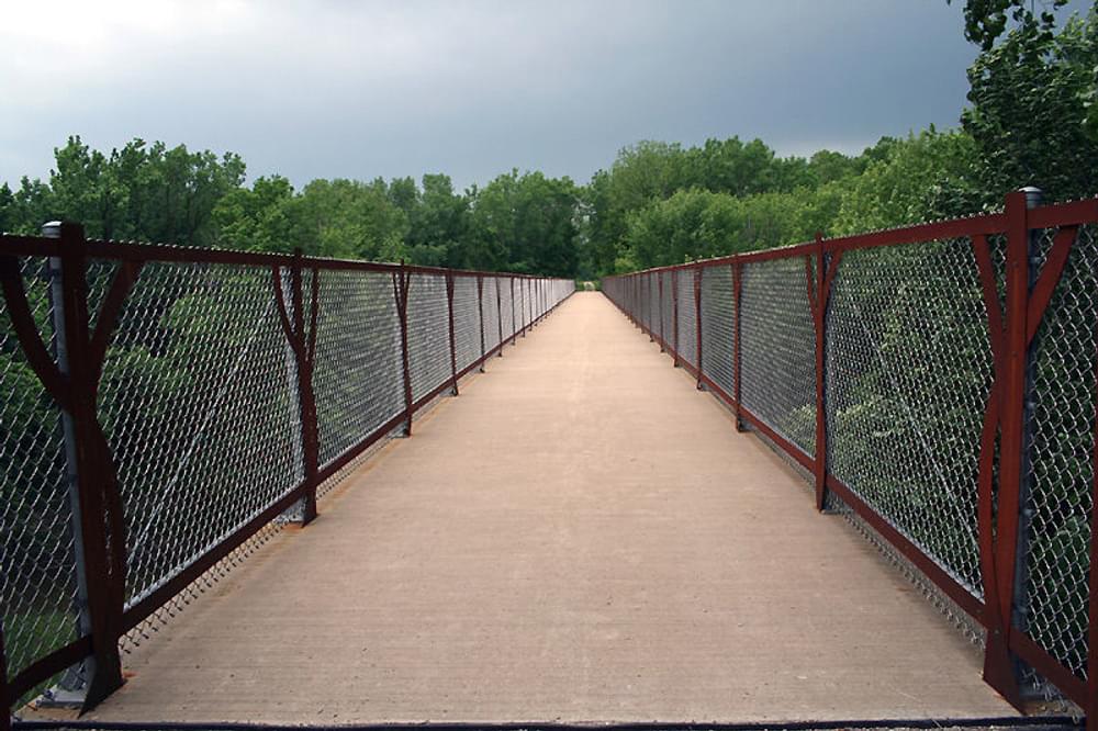 Cedar View Trail bridge. The four tree forms repeat throughout the 380 foot bridge, helping to visually connect the bridge to its environment and to frame the views of the creek and woodlands; Fairfield, IA; Artist: Judy Bales