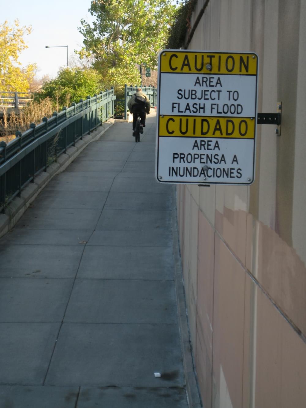 Sign in Spanish as well as English warns of possible flash floods along the Cherry Creek Trail in Denver, Colorado