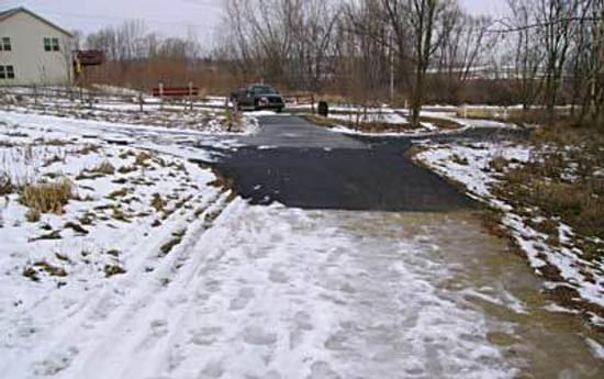 A test section shows how well snow has melted on the porous asphalt Section (center) compared to the crushed rock trail (foreground) and regular asphalt (far left and rear)