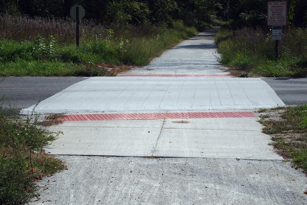 Concrete road crossing emphasizes crushed rock surface trail crossing paved road on Kal-Haven Trail in Michigan