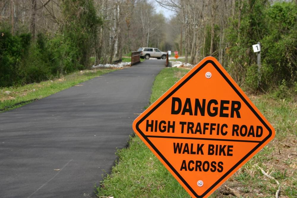 Serious warning sign about upcoming highway crossing in safety orange color on Swamp Rabbit Trail, Greenville, South Carolina