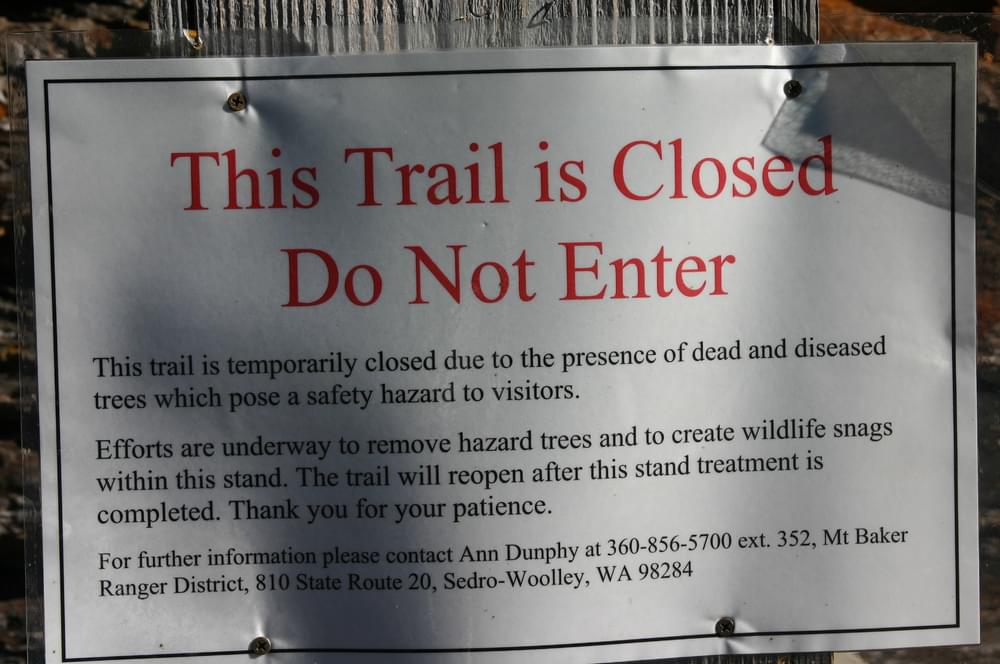 Detail of sign at Trail of the Sentinels trailhead; sign politely says why the trail is closed and who to contact for more information, including a person's name at Mt. Baker Ranger District, Washington