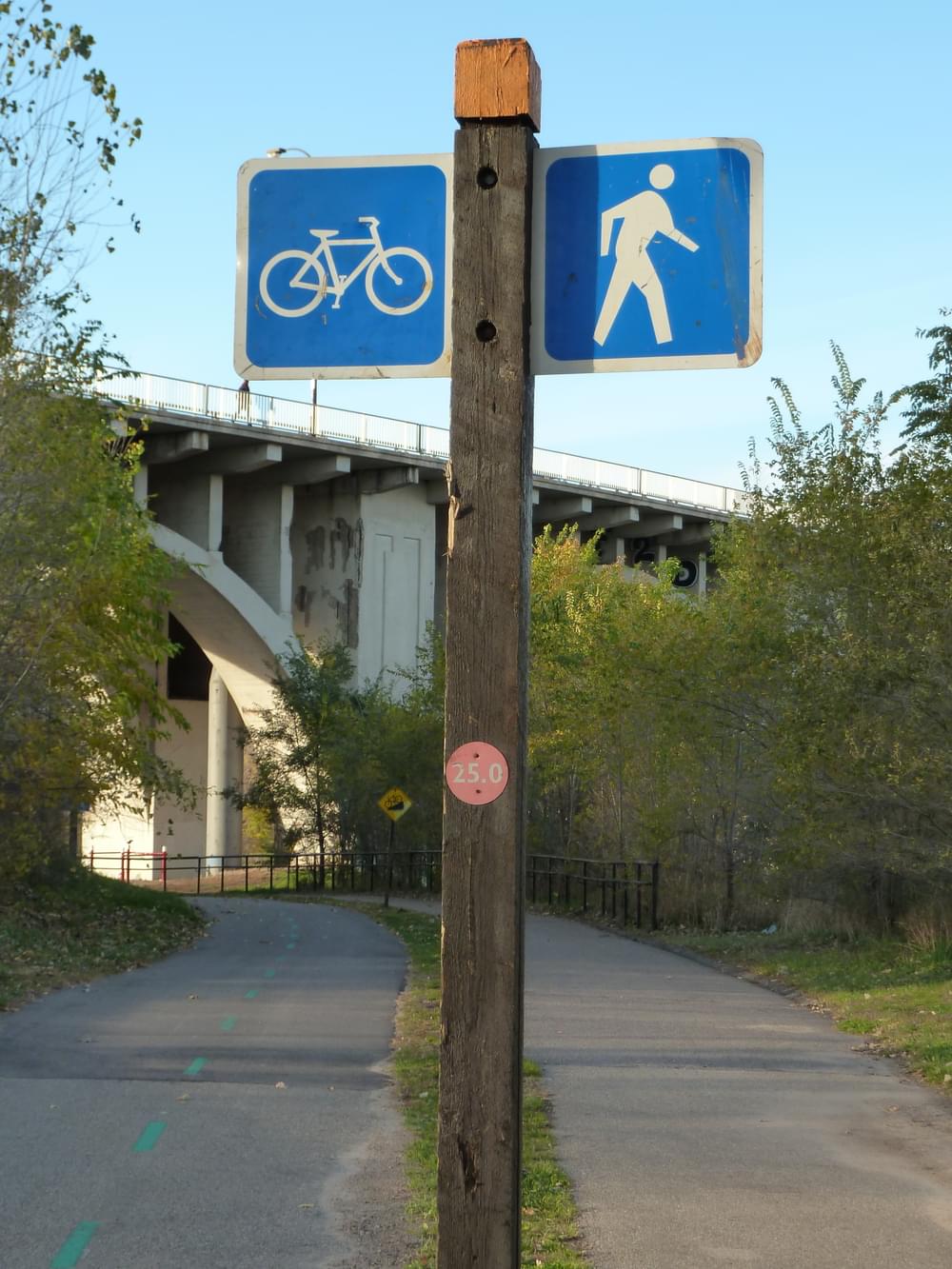 Signs between the bicycle and pedestrian routes on separated bicycle and pedestrian routes, both paved, along West River Parkway, Minneapolis