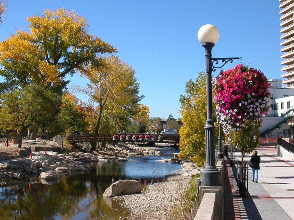 Concrete trail and planters along the embankment of the Truckee River in downtown Reno, Nevada; pedestrian bridge in the background, looking west 