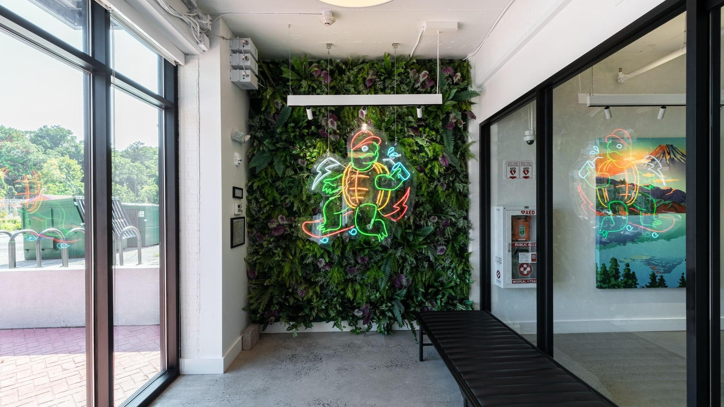 Vestibule at WeWork in College Park. A neon sign of Testudo the Terrapin riding a skateboard is surrounded by a soft green garden wall.